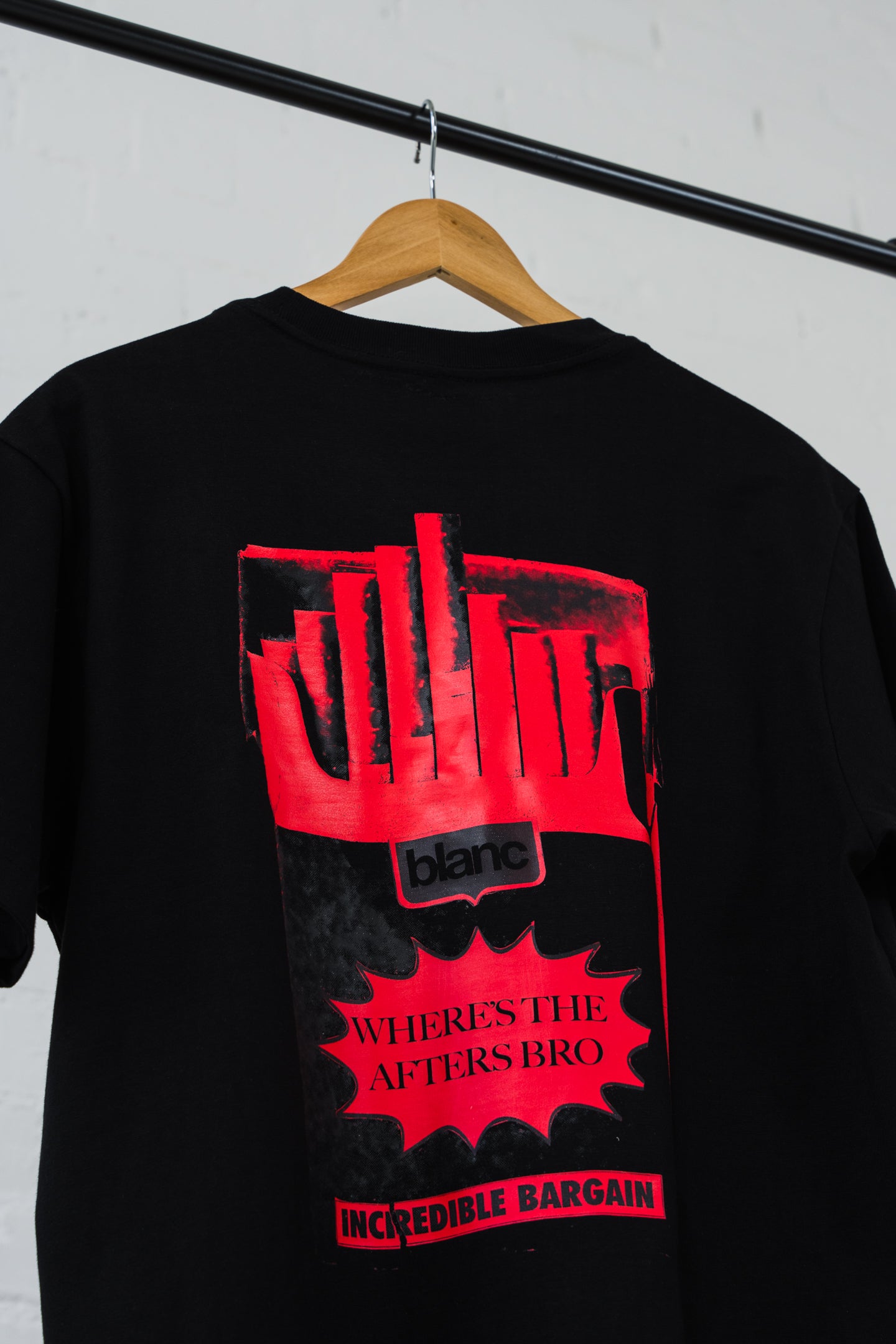 Black blanc t-shirt with red graphic design on a hanger against a white wall