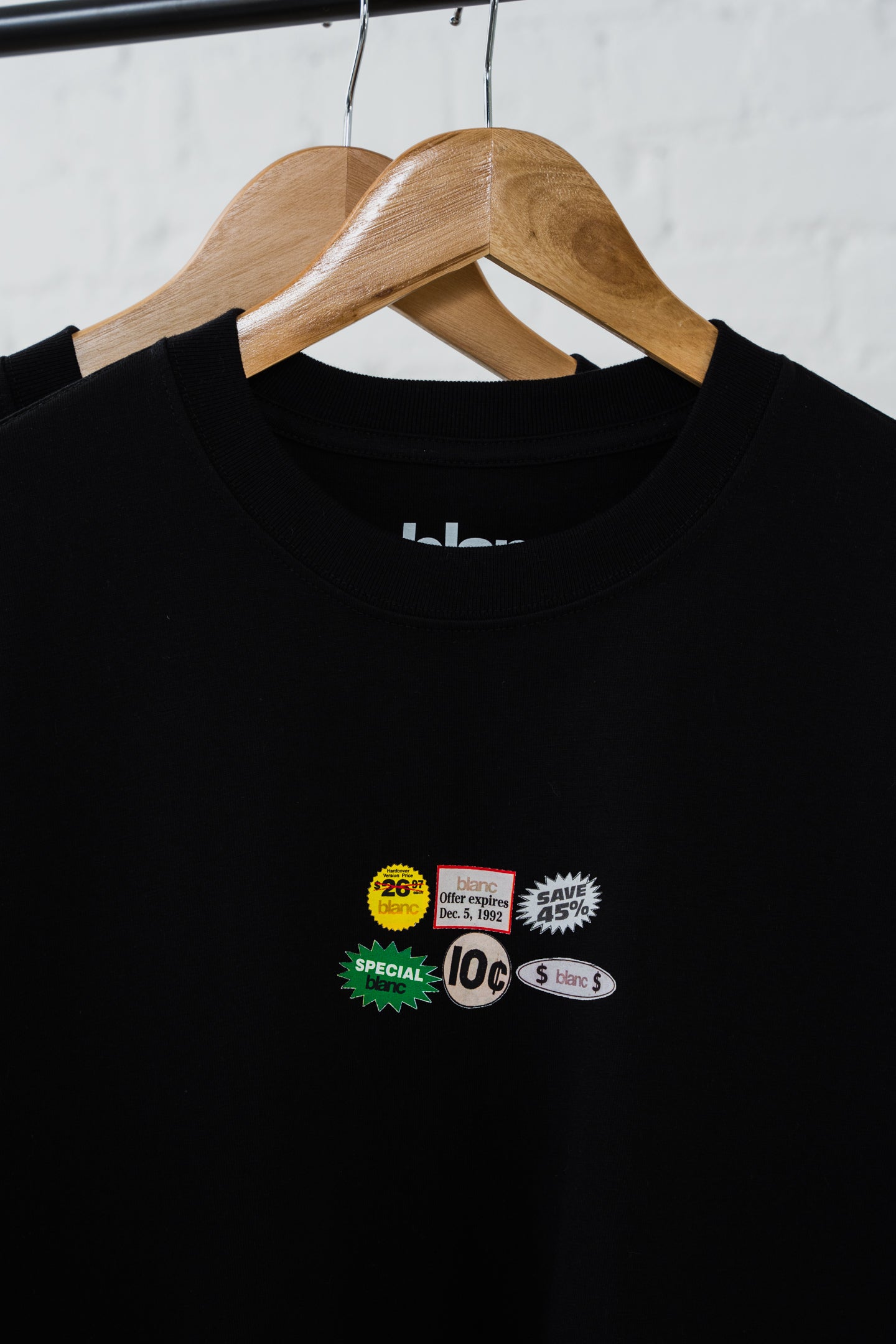 Black blanc T-shirt with vintage-style labels on a wooden hanger against a white background